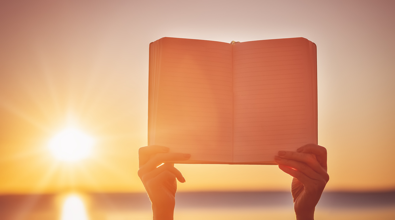 Hands gently holding an open journal with soft morning light, representing the beginning of a writing journey